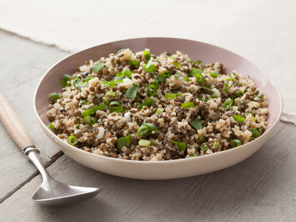 High-protein vegan lentil quinoa salad with green onions and fresh herbs in a bowl.