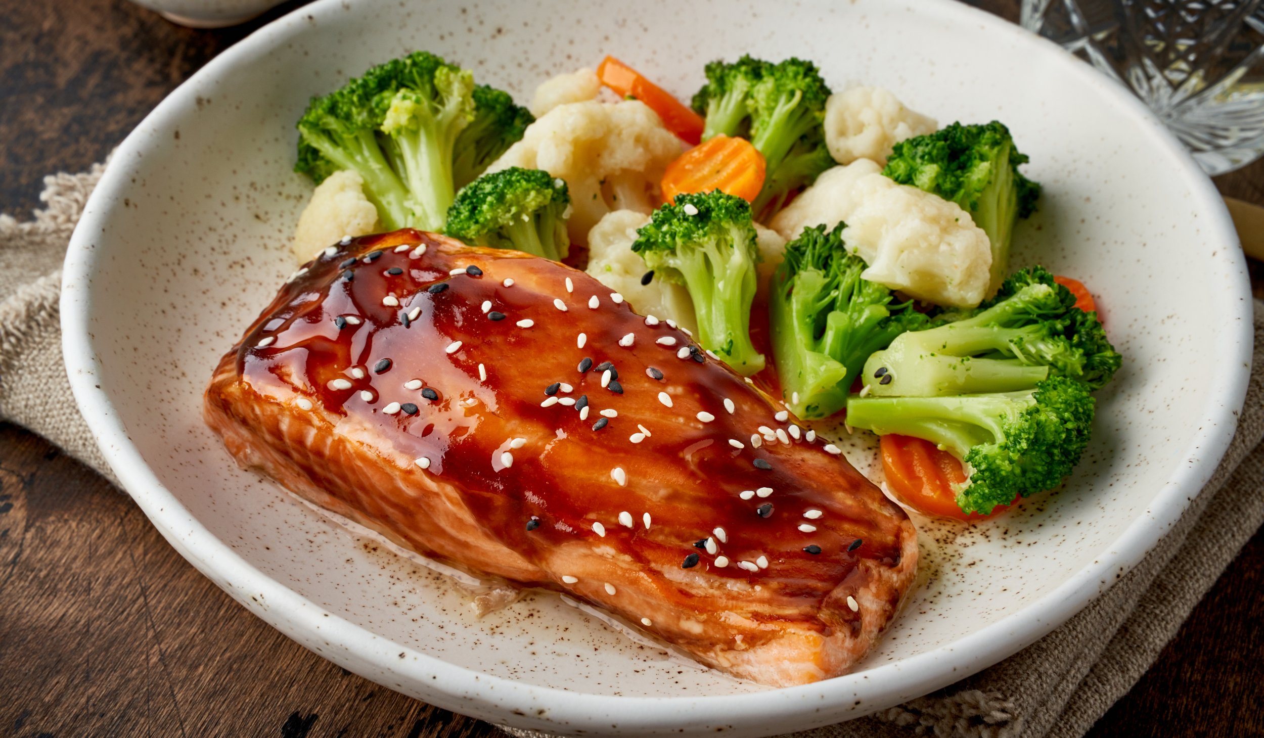 High-protein teriyaki salmon served with broccoli, cauliflower, and carrots in a ceramic bowl.