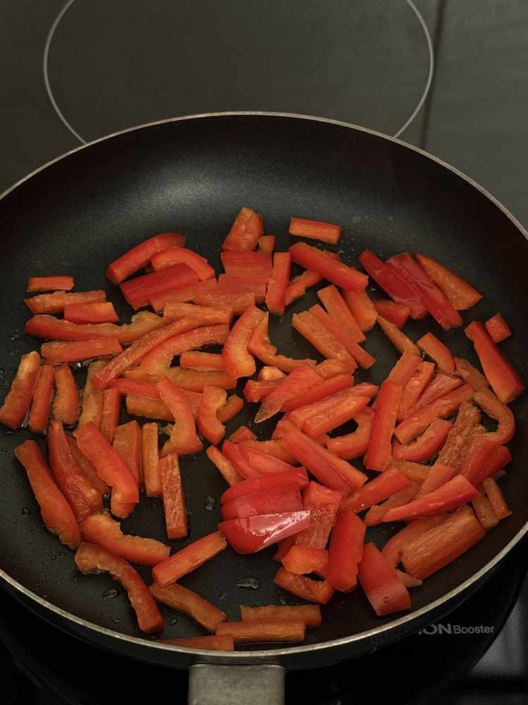Sliced red bell pepper sautéing in a pan