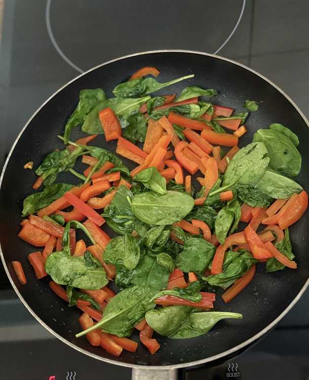 Fresh spinach wilting with sautéed peppers in a pan