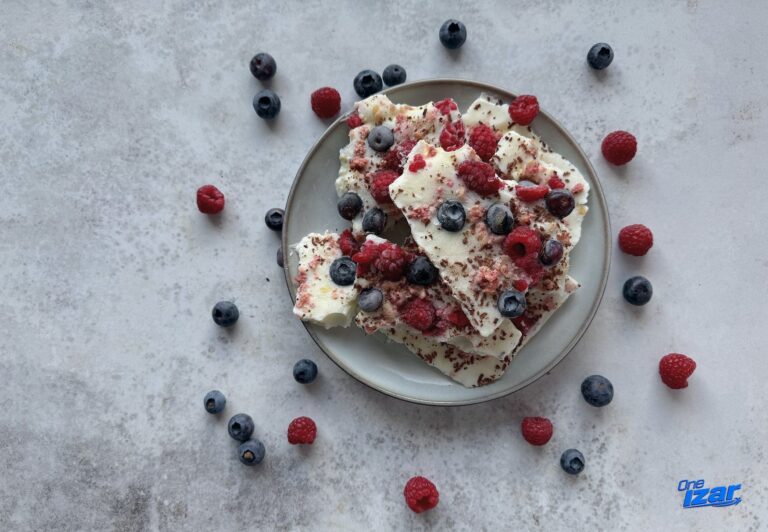 High-protein frozen berry yogurt bark topped with blueberries, raspberries, dark chocolate and granola, sliced into pieces on a plate